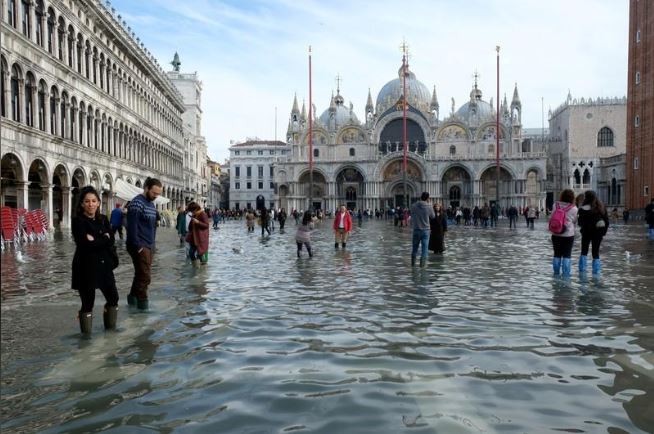 سياح يسيرون في ساحة القديس في مدينة البندقية الإيطالية وسط الفيضانات. تصوير: مانويل سيلفرستري - رويترز.